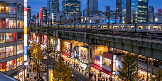 A commuter train passes above illuminated hobby shops and evening shoppers.
