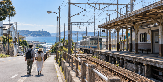 Two travelers walk beside a coastal railway station in Japan