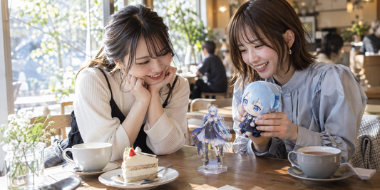 Two friends enjoy tea and cake with a character plush and acrylic stand at a cafe