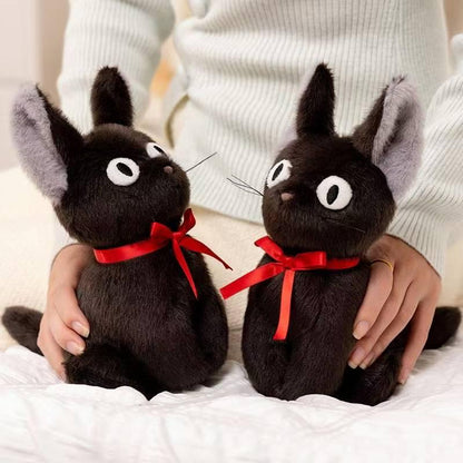 Two black cat plushes with red ribbons sitting on white bedding