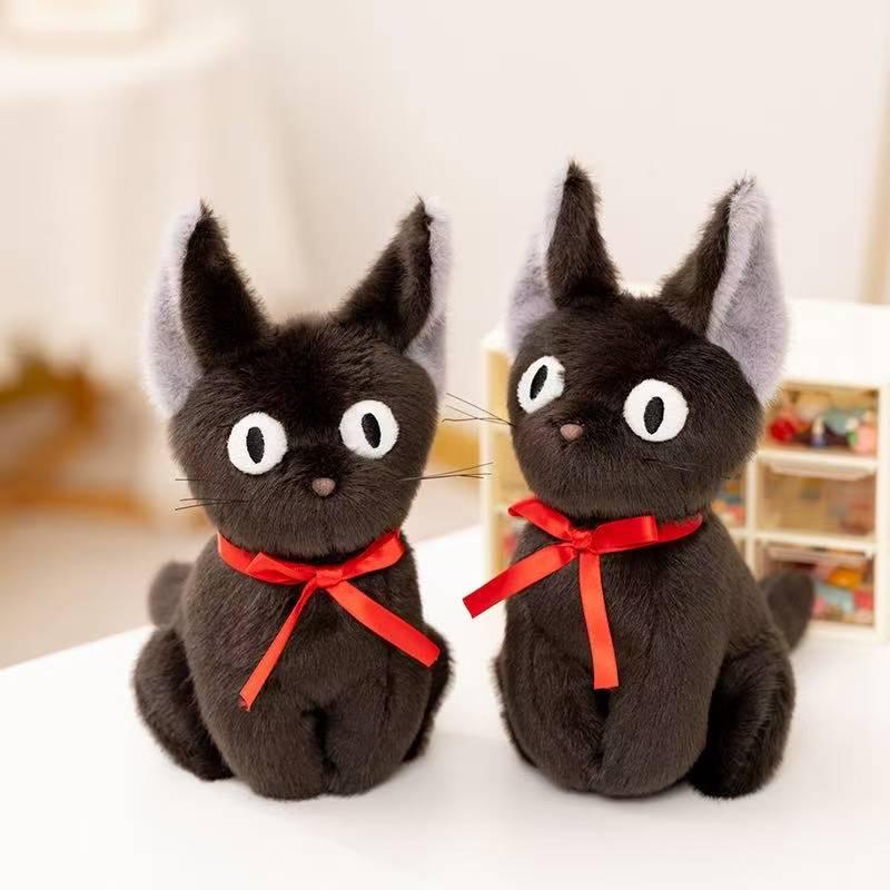 Two black cat plushes with red ribbons on a white table