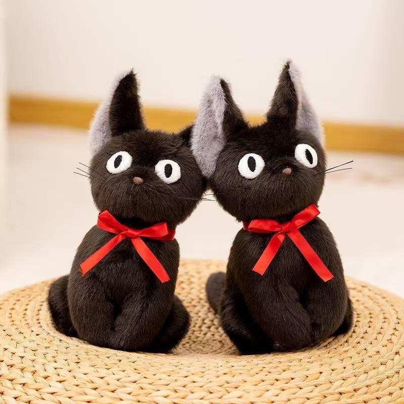 Two black cat plushes with red ribbons on a woven mat