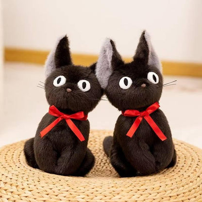 Two black cat plushes with red ribbons on a woven mat
