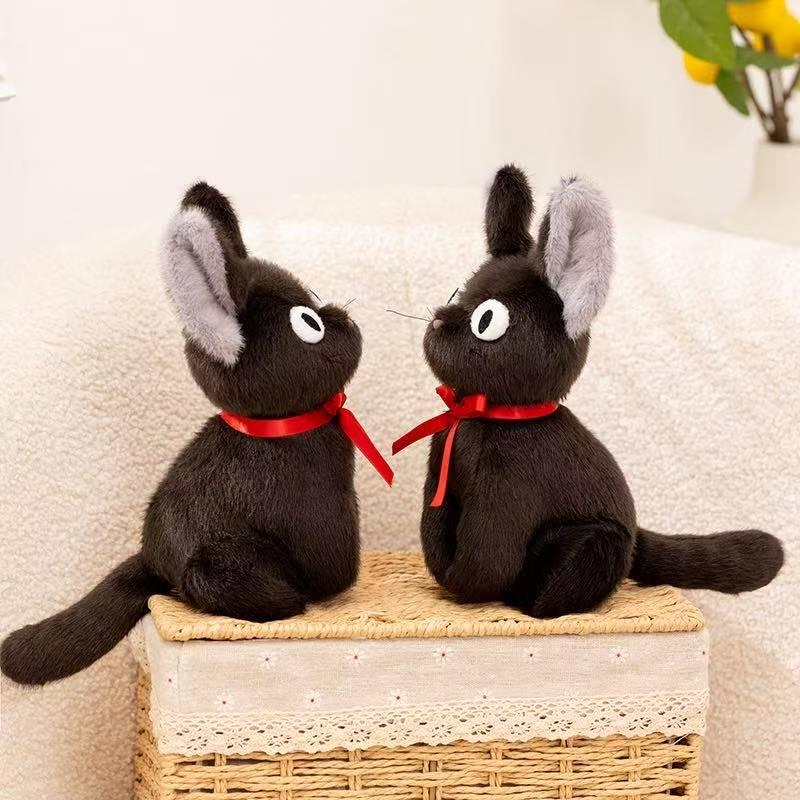 Two black cat plushes with red ribbons facing each other on a basket