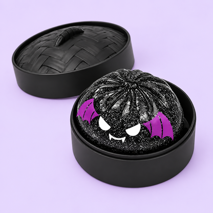 Spooky Bat Dumpling Squishy in its round case on a plain pastel lavender background